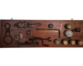4008 - Wooden Plaque w/ Ford & Vintage Car Parts (Description): Decorative wooden plaque featuring an  assortment of Ford and vintage automobile  parts mounted as wall art. The rich stained  wood board displays various antique car  components including gaskets, hub caps, a hand brace drill, wrench, and brass threaded  caps, some bearing the Dodge Brothers 'DB'  emblem. The arrangement creates an  interesting industrial assemblage piece.  Measures 12 1/2" x 36".