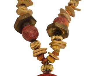 1486 - Beaded Necklace w/ Carved Cinnabar Pendant (Description): A 22" striking beaded necklace featuring a  large carved cinnabar pendant with  traditional Chinese longevity symbol (shou)  design. The necklace strand incorporates an  eclectic mix of beads including coral-colored spheres, gold-toned ribbed metal beads,  faceted brass beads, and natural bone  disc-shaped beads. The pendant displays  intricate carved scrollwork and geometric  patterns in deep red cinnabar.