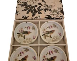 4046 - Set of 4 Chinese Garden Porcelain Ashtrays (Description): Set of Chinese Garden porcelain ashtrays  presented in their original decorative box.  The set includes four matching ashtrays, each  featuring hand-painted bird and floral  motifs with pink blossoms and peonies. The ashtrays have gold-trimmed rims and cigarette  rests. The original box displays a  coordinating black and white botanical  pattern with birds and reads "Chinese Garden  Porcelain Ashtrays."