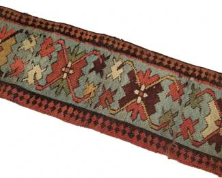 462 - Small Handwoven Kilim Table Runner 10"x30" (Description): Small handwoven kilim-style table runner  featuring traditional geometric and floral  motifs on a soft blue-gray field. The design  includes bold medallions in burgundy, rust  red, olive green, gold, and cream, framed by a decorative checkered border in black and  rust. The piece shows characteristic  hand-knotted wool construction with visible  fringe at the ends. Measures 10 inches by 30  inches.