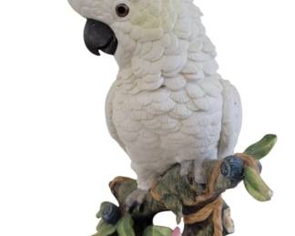 429 - Cockatoo Figurine on Floral Branch 11" (Description): A decorative figurine depicting a white  cockatoo with yellow crest perched on a  naturalistic branch base adorned with pink  flowers, green foliage, and blue berries. The  piece features detailed feather texturing throughout the bird's plumage. Sold as is.  Measures 11 inches tall.