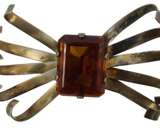 1913 - Sterling Art Deco Ribbon Brooch 0.95oz (Description): Sterling silver Art Deco ribbon brooch  featuring a large faceted amber-colored glass  stone at the center. The brooch has a  distinctive bow or ribbon design with curled  ends radiating outward from the central stone. Weight is 0.95oz.