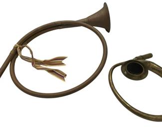964 - Two Decorative Brass French Hunting Horns (Description): Two decorative brass French hunting horns of  different sizes. The larger horn features a  wide circular coil with a flared bell and  straight mouthpiece, adorned with a  decorative striped ribbon bow. The smaller horn has a compact single-coil design with a  traditional bell shape. Both display a warm  patinated brass finish characteristic of  vintage decorative horns.