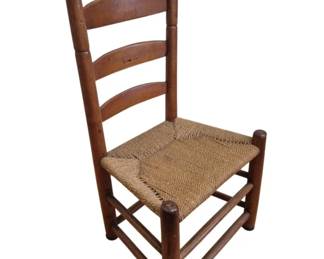 1284 - Antique Ladderback Chair w/ Rush Seat (Description): Antique ladderback chair featuring a woven  rush seat. The chair has turned wooden posts  with ball finials at the top, three curved  horizontal slats forming the ladder back, and  sturdy stretchers connecting the legs for support. The wood displays a warm, aged  patina consistent with period furniture.  Measures 36" x 19" x 15".