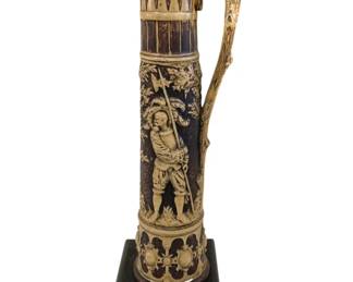 394 - Antique Tall Decorative Pitcher on Wood Stand (Description): Possibly Bretby Art Pottery in England, tree  branch handle, relief figure of soldier or  guard holding a halberd, surrounded by  foliage. 25" tall x 7"