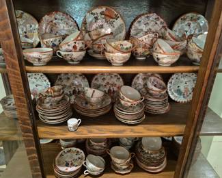 4002 - Group Lot of Assorted Asian Porcelain (Description): A large group lot of assorted Asian porcelain  featuring hand-painted figural and floral  designs. The collection includes numerous  cups and saucers, plates, bowls, and  decorative pieces in various sizes. Many pieces display traditional Japanese Geisha  and landscape scenes with characteristic  orange-red borders and gilt accents. The  porcelain exhibits the delicate hand-painted  style typical of Japanese Kutani and Satsuma