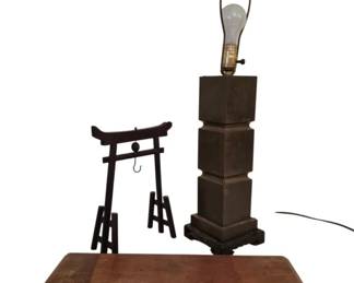 3993 - 3 Pcs. Oriental Items Lamp Stand & Gong (Description): A collection of three Oriental-style items  comprising a stacked cube table lamp with  brass or bronze finish on a decorative base,  a small iron torii gate-style gong frame with  hook, and a low wooden display stand or tray with curved scroll feet. The lamp features a  tiered design of graduated cubes and  includes a harp. The wooden stand shows  rustic character and patina consistent with  age.