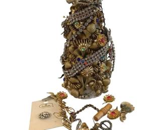 381 - Christmas Tree Made from Costume Jewelry (Description): A decorative Christmas tree crafted from  costume jewelry and brooches. The tree  features an assortment of rhinestone pieces,  colorful gemstone brooches, and gold-toned  jewelry elements arranged in a festive conical shape. Measures 9 inches tall.