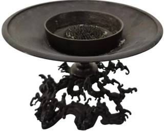 303 - Japanese Bronze Ikebana Wave Vase & Metal Frog (Description): Japanese Bronze Vase featuring a wide rimmed  dish top with a central recessed bowl  containing a flower frog insert. The piece is  supported by an elaborately sculpted base  designed to resemble organic, twisted branches, roots or waves, creating a natu
