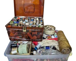 4085 - 2 Boxes Full of Sewing Thread & Notions (Description): Two boxes full of sewing thread and assorted  notions. The collection includes a vintage  amber-colored plastic sewing box with  fold-out compartments filled with spools of  thread in various colors, along with a larger plastic storage container containing  additional thread spools, crochet thread and  other sewing supplies. A substantial  collection suitable for the avid seamstress  or crafter.