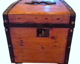 614 - Vtg Wood Trunk w/ Metal Straps 17"x16"x17" (Description): Vintage small wooden trunk featuring metal  corner straps and edge banding secured with  brass-finished studs. The trunk has a hinged  lid with a decorative metal handle plate and  a front latch closure. The wood shows a warm reddish-brown patina with natural wear  consistent with age and use. Measures 17  inches by 16 inches by 17 inches.