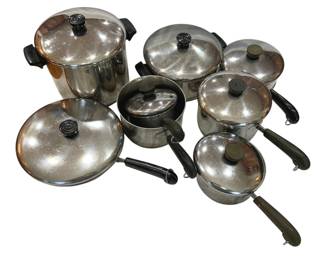 923 - Revere Cookware Set with Lids (Description): A comprehensive stainless steel pot and pan  set featuring multiple pieces with matching  lids. The collection includes various sized  pots and pans with black phenolic handles,  suitable for a range of cooking needs. The cookware shows signs of use consistent with a  well-loved kitchen set.
