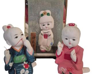 3948 - 3 Oriental Figurines 8"x5"x4" (Description): Three oriental figurines featuring children  in traditional Asian attire. The collection  includes two ceramic figures dressed in  colorful kimonos—one in blue with floral  patterns and one in pink with peony designs—and a third figure in original box  depicting a child in white garments. Each  figure displays hand-painted details and  traditional hairstyles. Measures 8" x 5" x  4".