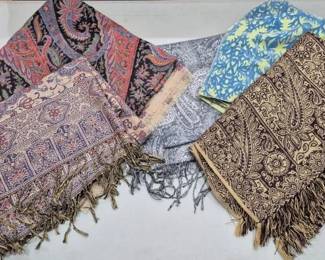 2857 - Collection of Five Fringed Scarves (Description): A collection of five decorative scarves  featuring various patterns and designs. The  grouping includes paisley prints in rich  jewel tones, a geometric bordered scarf with  fringe detailing, a gray and white paisley print with fringe, a blue and yellow floral  pattern scarf, and a brown and black ornate  paisley design with fringe. Several of the  scarves feature traditional fringed edges.