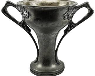 177 - John Frick Jewelry Company Silver Plate Trophy (Description): A silver plate trophy by John Frick Jewelry  Company featuring ornate dual handles with  foliate decorative elements. The trophy has a  flared trumpet-form body rising from a  circular base. Measures 11.5" x 13" x 9".