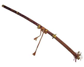 2717 - Kitani Sword w/ Decorative Scabbard (Description): Kitani sword featuring an ornate scabbard  with red and gold brocade covering adorned  with decorative metalwork. The handle is  wrapped in traditional cord binding with  gold-toned fittings and tasseled accents. The scabbard includes a braided cord with  tassels for carrying. The sword displays  characteristic Japanese craftsmanship with  gilt metal mounts throughout.