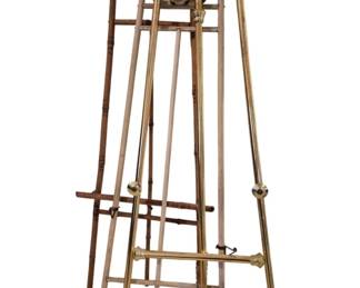 3748 - 4 Vtg Easels Brass Wood & Painted Metal 60" (Description): Collection of four vintage easels measuring  60 inches tall. The group includes one brass  easel with decorative turned details and ball  feet, two wooden easels with faux bamboo  styling and scrolled finials, and one painted metal easel. All feature traditional A-frame  construction with adjustable canvas  supports, suitable for displaying artwork or  decorative items.
