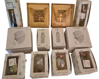 4065 - 14 Silvestri Ornaments in Original Boxes (Description): Collection of fourteen Silvestri ornaments,  all in their original boxes. The assortment  includes decorative butterfly figures,  iridescent glass ornaments, whimsical figural  designs featuring angels or fairies with elaborate wings, and novelty shapes. Several  boxes display the Silvestri logo with  snowflake graphics. The ornaments feature  various finishes including metallic gold  tones and iridescent glass effects.