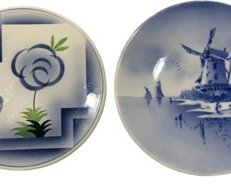 993 - 2 Blue & White Decorative Plates 12"x13.5" (Description): Two decorative plates in blue and white. One  features a stylized floral design with  abstract cloud-like flowers and green leaves  against a geometric background. The other  displays a traditional Dutch windmill scene with a landscape reflected in water. Measures  12".