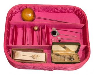 1971 - Group of Vintage Hatpins & Stick Pins (Description): A collection of vintage flat pins including  hatpins and stick pins. The group features  various decorative styles including a  monogrammed gold-tone bar pin in its original  presentation box, an amber-colored faceted dome hatpin, a faux pearl topped pin, and  several other decorative pins with assorted  finishes and ornamental heads. Some pins  retain their original vintage cases.  Displayed in a pink quilted satin pin holder.