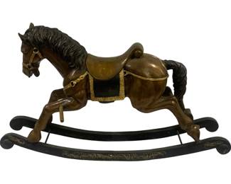 8006 - Bronze Rocking Horse 48"x17.5"x28" (Description): Bronze rocking horse featuring a galloping  pose with finely detailed mane and tail. The  horse is outfitted with a golden brass-toned  saddle accented with decorative fringe trim  and bridle with brass fittings. Mounted on a black lacquered curved wooden rocker base  embellished with elegant gilt scrollwork  ornamentation at each end. Measures 48 inches  long by 17.5 inches wide by 28 inches high.