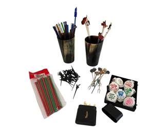 568 - Lot of Swizzle Sticks & Cocktail Forks (Description): An assorted lot of swizzle sticks and  cocktail forks. The collection includes glass  swizzle sticks in various colors, decorative  figural cocktail picks with animal and  character toppers, black plastic sword picks, plastic swizzle sticks in red and green,  metal cocktail forks, novelty bottle stoppers  with humorous sayings, and two horn cups  used for storage. A diverse barware  collection suitable for entertaining.
