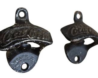 4052 - 2 Vtg Cast Iron Coca-Cola Wall Mount Openers (Description): Two vintage cast iron Coca-Cola wall mount  bottle openers. These black painted openers  feature the classic embossed Coca-Cola script  logo and include mounting holes for wall  installation. One opener is marked 'Starr X' on the lower portion, indicating the  well-known Brown Manufacturing Company  design. Both show patina and wear consistent  with age and use.