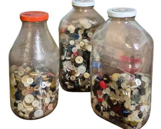 4109 - 3 Vintage Glass Jars Filled with Buttons (Description): Collection of three vintage glass jars filled  with assorted buttons. The jars include two  larger bottles with white metal lids and one  smaller bottle with an orange lid. The  buttons are of various sizes, colors, and materials, ranging from mother of pearl and  shell to plastic and metal, in shades of  white, cream, black, red, blue, and brown. An  excellent collection for crafters,  seamstresses, or collectors of vintage sewing