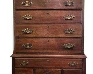 3810 - Queen Anne Style Mahogany Highboy Chest (Description): A Queen Anne style mahogany highboy chest of  drawers in one piece construction. This  elegant piece features a distinctive broken  pediment top with carved rosettes and a  central urn finial. The upper section contains seven graduated drawers with brass  bail pulls and escutcheons, while the lower  section features one long drawer over three  smaller drawers with matching brass hardware.  The piece rests on graceful cabriole legs