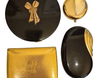 1496 - Vtg Gold Tone & Black Enamel Compact Lot (Description): A collection of four vintage compacts and  cases featuring gold tone and black enamel  finishes. The lot includes a round black  enamel compact with an applied gold tone bow  adorned with rhinestones, a small round gold tone compact, an oval black enamel compact  with a decorative gold tone leaf motif, and a  rectangular gold tone case with an engraved  monogram on a textured surface. A lovely  assortment of mid-century vanity accessories.