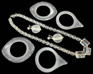 2812 - Group Mid-Century Clear Lucite Jewelry (Description): Group of clear Lucite jewelry pieces  including four geometric teardrop-shaped  bangless with circular cutouts, a beaded cube  necklace with barrel clasp pendant, and a  pair of screw-back earrings with faceted globe drops.