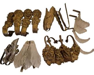 4040 - Group Metal Glass & Acrylic Curtain Tie Backs (Description): A collection of ornate curtain tie backs in  various materials including metal, glass, and  acrylic. The grouping features gilt metal  tie backs with elaborate grape and leaf  cluster designs, clear ribbed glass shell-form tie backs with metal mounting  brackets, and an acrylic leaf-form example.  The pieces exhibit a decorative castle or  estate style suitable for formal drapery  presentations.