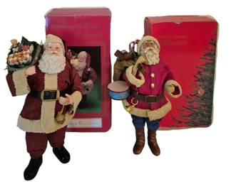 4061 - 2 Clothtique Santa Claus Figures w/ Boxes (Description): Two Santa Claus figures with their original  boxes. One is from the Possible Dreams  Clothtiques collection featuring Santa in a  magenta coat with cream trim, carrying a sack  of toys and a drum. The second is from the Windsor Collection Fabric Mache Santa  Collectibles line, depicting Santa in a  burgundy suit with cream-colored trim,  holding a lantern and carrying a sack filled  with presents. Both figures feature detailed