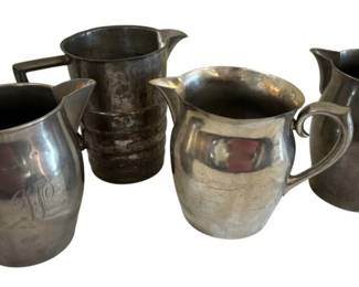 569 - 4 Pewter & Other Pitchers 7.5" (Description): Collection of four pitchers in pewter and  other metals. The grouping includes varied  styles with curved handles and classic  pitcher forms. One pitcher features an  engraved monogram. The tallest measures 7.5 inches.