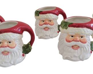 458 - 5 Ceramic Santa Head Christmas Mugs 5"x5" (Description): Set of five ceramic Santa head mugs featuring  hand-painted details. Each mug depicts  Santa's cheerful face with rosy cheeks, white  beard, and red hat, accented with green  holly leaves. The Santa hat forms the handle of each mug. Measures 5" x 5".