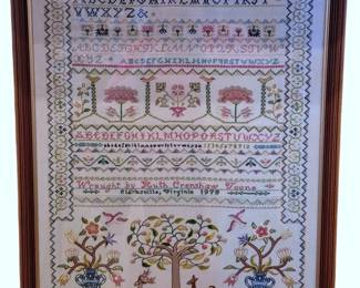 611 - Framed Needlework Sampler 25"x19" (Description): A framed needlework sampler featuring  traditional alphabet rows, numbers, and  decorative motifs. The piece includes floral  designs, trees, birds, and urns with flowers  worked in cross-stitch on a light ground. The right portion displays a charming pastoral  scene with fruit trees and flowering urns  against a golden background. The sampler is  signed and dated 1979. Presented in a wooden  frame with gilt inner border. Measures 25