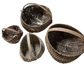 4127 - 4 Vintage Woven Egg Baskets (Description): Collection of four vintage woven egg baskets  with bent wood handles. The baskets feature  traditional splint weave construction in  varying sizes, displaying a natural aged  patina. Each basket has the characteristic rounded form and sturdy overhead handle  typical of gathering baskets. The set  includes one large basket, two medium  baskets, and one small basket, all showing  authentic wear consistent with age and use.