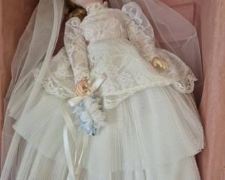 1391 - Madame Alexander Elise Bridesmaid Doll #1685 (Description): Elise Bridesmaid doll, model #1685. The doll  measures 17 inches in height and is presented  in its original box with pink tissue paper.  She wears an elegant bridal ensemble  featuring a lace bodice, tulle skirt, and flowing veil, and holds a delicate floral  bouquet with blue flowers and ribbon accents.