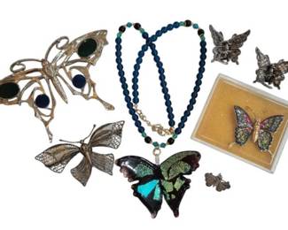 1977 - Group of Butterfly Themed Jewelry (Description): A collection of butterfly themed jewelry  pieces including brooches, a beaded necklace  with butterfly pendant, and pins. The  assortment features various styles and  finishes including gold-tone, silver-tone, and filigree work, with some pieces  incorporating colorful enamel and glass  cabochon accents. A decorative grouping for  butterfly enthusiasts or costume jewelry  collectors.