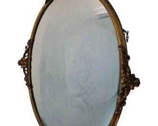 3752 - Ornate Gilt Metal Frame Oval Mirror 23"x16" (Description): Oval mirror with an ornate gilt metal frame  featuring decorative rococo-style scrollwork  and floral accents at the corners. The frame  displays a warm brass or bronze-toned finish  with intricate cast details.