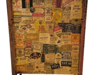 3969 - Vtg Wooden Bar Cabinet w/ Liquor Label (Description): Vintage wooden bar cabinet featuring a  decorative collage of liquor and spirit  labels on the front panel. The cabinet  displays an eclectic array of brand labels  including Beefeater, Jim Beam, Jack Daniel's, Gordon's Gin, Cutty Sark, Smirnoff,  Hennessey, and many others from the mid-20th  century. The piece has a worn red-painted  finish with natural wood showing through,  giving it authentic aged character. Measures