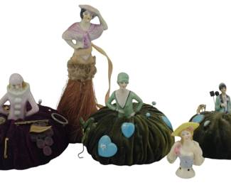 893 - Assorted Decorative Pin Cushions & Brush (Description): Assorted decorative pin cushions featuring  porcelain half-doll figures. The collection  includes various styles with velvet cushion  bases in deep burgundy and olive green tones.  Several half-dolls are dressed in period attire, and some cushions contain pins and  sewing notions.