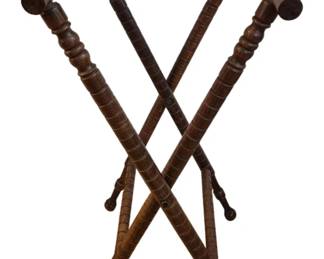 300 - Antique Wooden Folding Butler Tray Stand (Description): Antique wooden folding butler tray stand  featuring turned spindle legs with decorative  ring details. The X-frame design allows for  easy folding and storage. The top is fitted  with woven fabric straps to support a serving tray. The dark wood finish sh