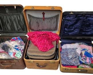4103 - 3 Vintage Suitcases with Assorted Fabric (Description): Three vintage suitcases filled with assorted  fabric. The collection includes a brown  leather-trimmed suitcase, a tan tweed-style  suitcase, and a navy blue suitcase, each  featuring fabric-lined interiors. The suitcases contain various fabrics including  floral prints, polka dots, and patchwork  quilting materials in an array of colors and  patterns.