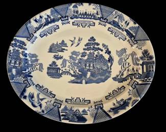 502 - Johnson Bros Blue & White Willow Platter (Description): A blue and white transfer-printed platter  featuring the classic Willow pattern design.  The oval platter displays a traditional  chinoiserie scene with pagodas, bridges,  birds in flight, and stylized landscape elements. The wide rim is decorated with  architectural vignettes and scrollwork  borders containing text banners. Measures  16.5" x 14".