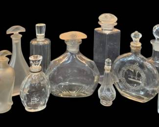 1467 - Vtg Clear & Frosted Glass Perfume Bottles (Description): A collection of vintage clear and frosted  glass perfume bottles in various sizes and  styles. The assortment includes bottles with  faceted crystal stoppers, frosted glass  stoppers, and decorative pressed glass designs. Several feature elegant shapes  including round flattened forms, rectangular  bottles, and classic tapered silhouettes. One  bottle displays an etched wreath design. The  collection showcases a variety of vanity
