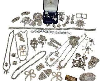 2710 - Group Paste & Costume Jewelry Collection (Description): A diverse collection of paste and costume  jewelry featuring an array of rhinestone and  crystal-set pieces. The grouping includes  brooches, necklaces, bracelets, earrings,  shoe buckles, and decorative clips in various Art Deco and mid-century styles. Notable  pieces include floral sprays, geometric  designs, bow motifs, and starburst patterns.  The collection presents predominantly  silver-toned settings with clear and