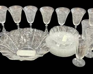 1256 - Fostoria Corsage Etched Crystal Glassware Set (Description): A collection of Fostoria Corsage pattern  etched crystal glassware. The set includes  various stemware pieces such as water  goblets, wine glasses, and cordial glasses,  all featuring the delicate Corsage etching pattern with floral and scroll motifs. Also  included are etched salad plates and a  decorative fan-shaped serving dish in the  coordinating pattern. The elegant etched  design is characteristic of Fostoria's