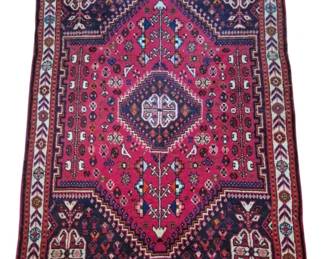 2802 - Vtg Persian Style Hand-Knotted Wool Rug (Description): Vintage Persian style hand-knotted wool rug  featuring a traditional medallion design. The  rug displays a vibrant red/magenta central  field with a geometric diamond medallion,  surrounded by intricate tribal motifs in navy blue, cream, orange, and turquoise. The  design includes stylized floral and animal  figures throughout. A cream border with  repeating arrow and floral patterns frames  the piece, finished with fringe at both ends.