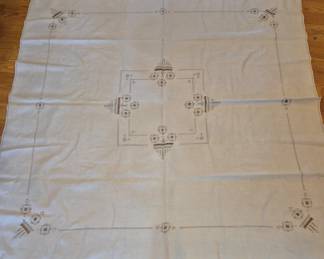 1458 - Vtg Embroidered Linen Tablecloth 68"x68" (Description): Vintage cream-colored linen tablecloth  featuring delicate cross-stitch embroidery in  muted brown and tan tones. The design  includes ornamental motifs arranged  symmetrically around a central medallion, with coordinating corner decorations.  Hemstitched borders frame the piece, adding  elegant detail.